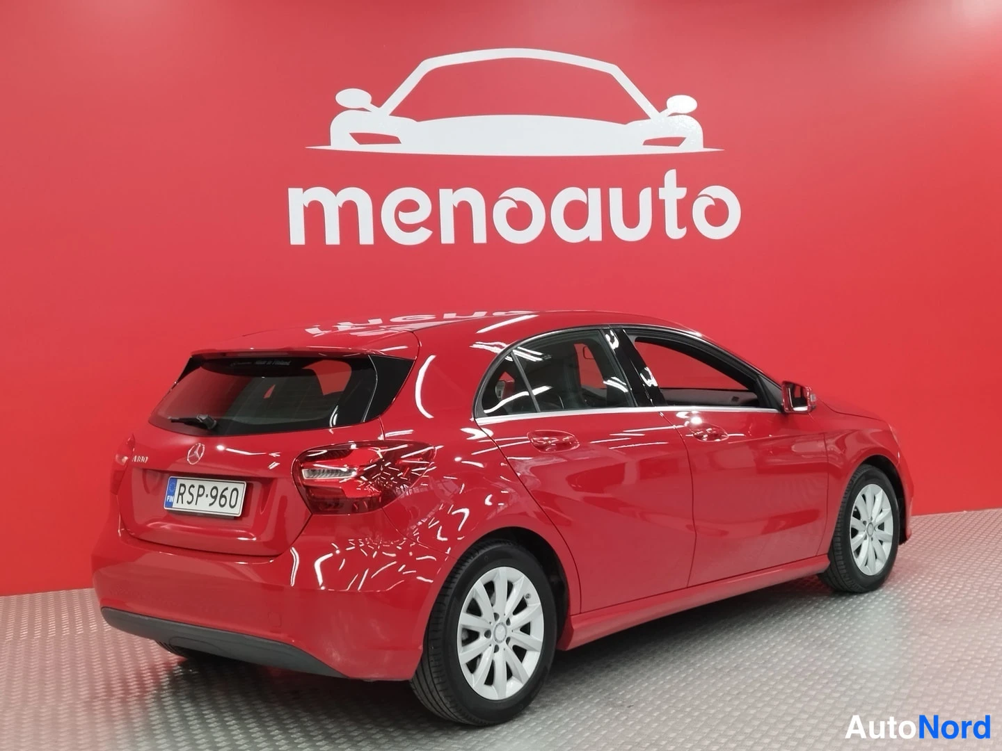 Takaviisto: Punainen Mercedes-Benz A -mallinen viistosti takaa vasemmalta kuvattu auto, rekisterikilpi, punaisella menoauto-taustalla.