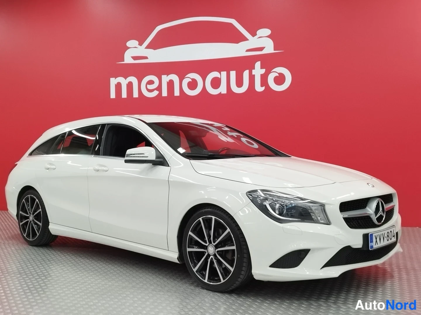 Etuviisto, nokka oikealle: Valkoinen Mercedes-Benz CLA Shooting Brake etukulmasta punaisella taustalla