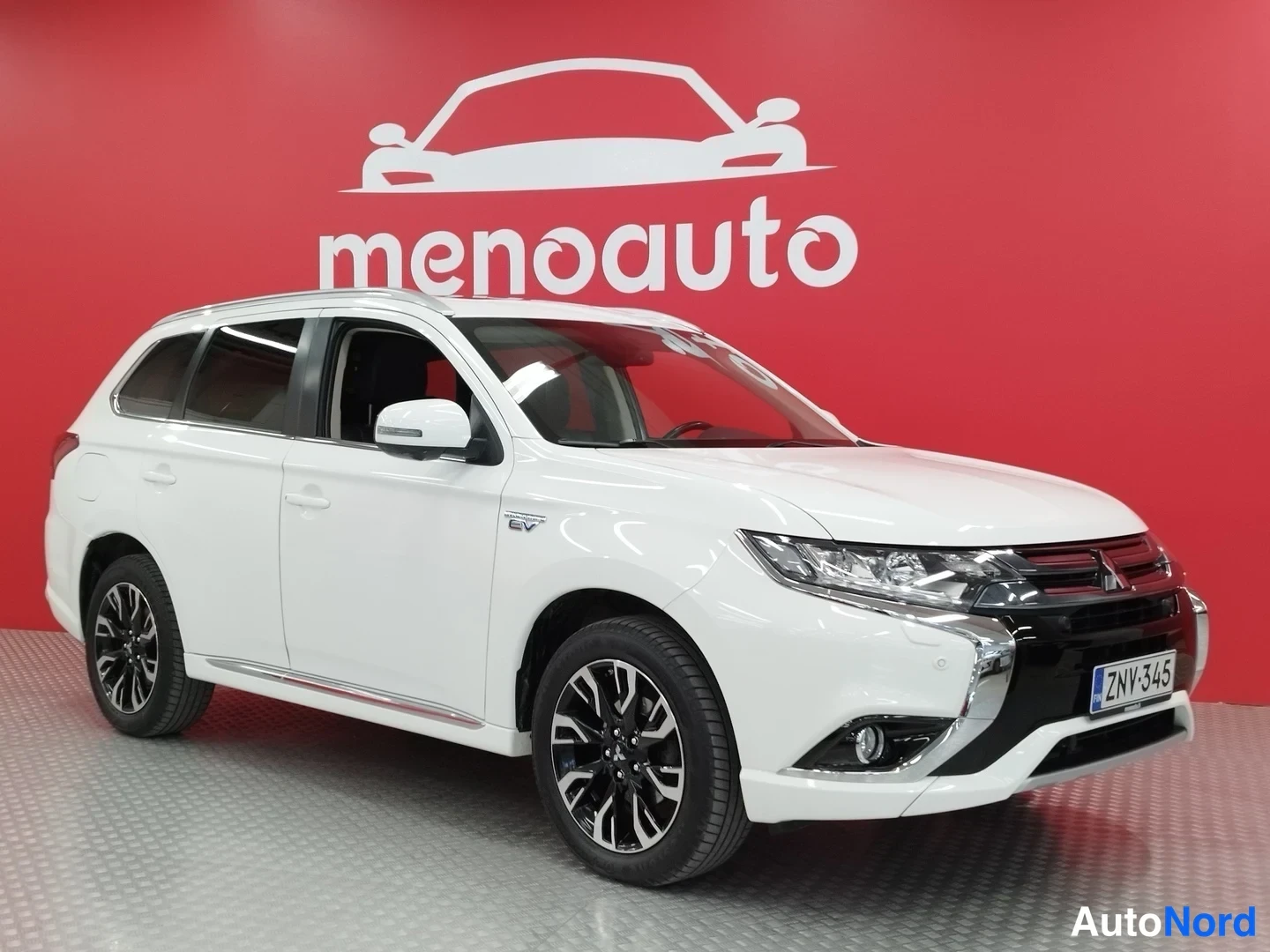 Etuviisto, nokka oikealle: Valkoinen Mitsubishi Outlander PHEV edestä oikealta kuvattuna punaisella menoauto-taustalla.