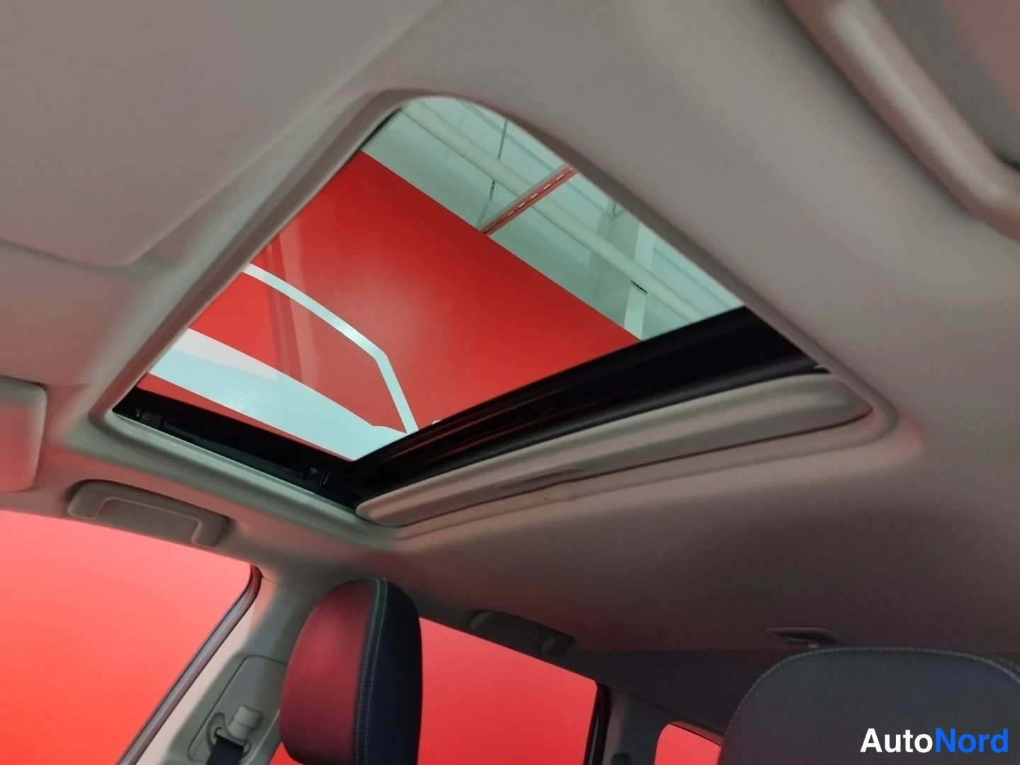 Yksityiskohta: Auton sisätilat: aukeava panoraamakatto (sunroof), vaalea katto ja punamusta taustaseinä.