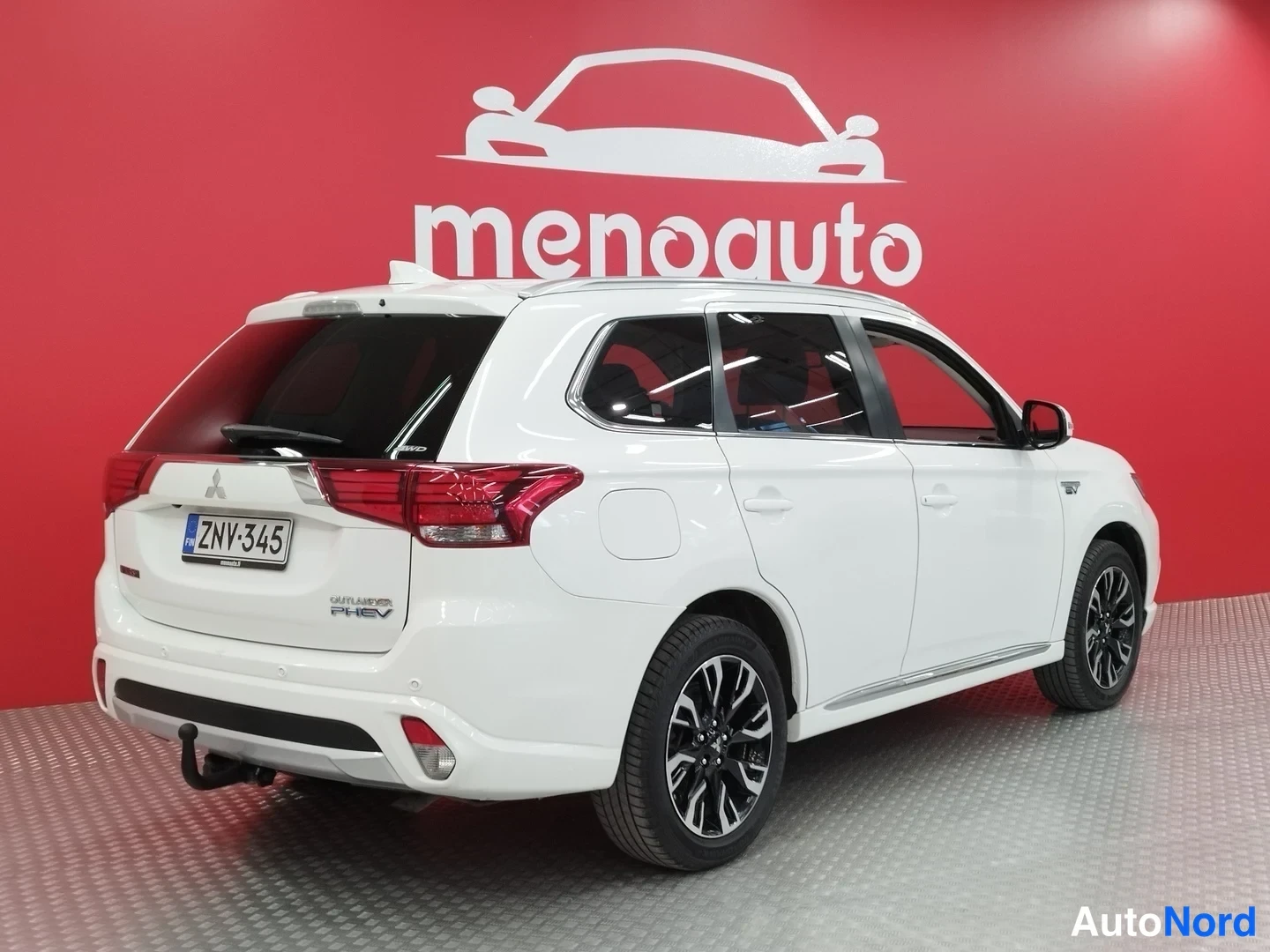 Takaviisto: Valkoinen Mitsubishi Outlander PHEV takaa vasemmalta kuvattuna punaisella menoauto-taustalla.