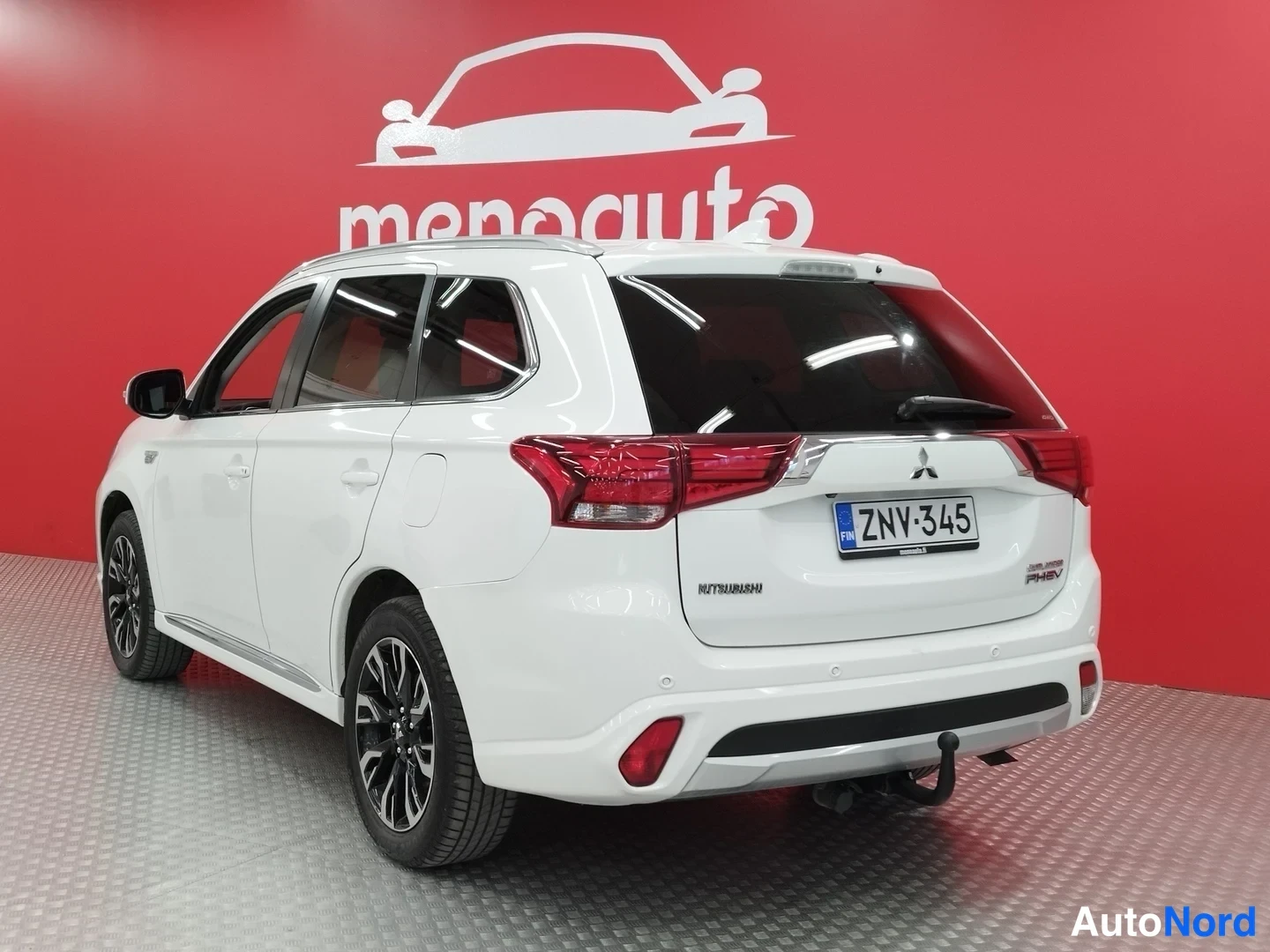 Takaviisto: Valkoisen Mitsubishi Outlanderin takakolmasosanäkymä, rekisteritunnus, punainen merkkipaneeli ja vetokoulu näkyvät.