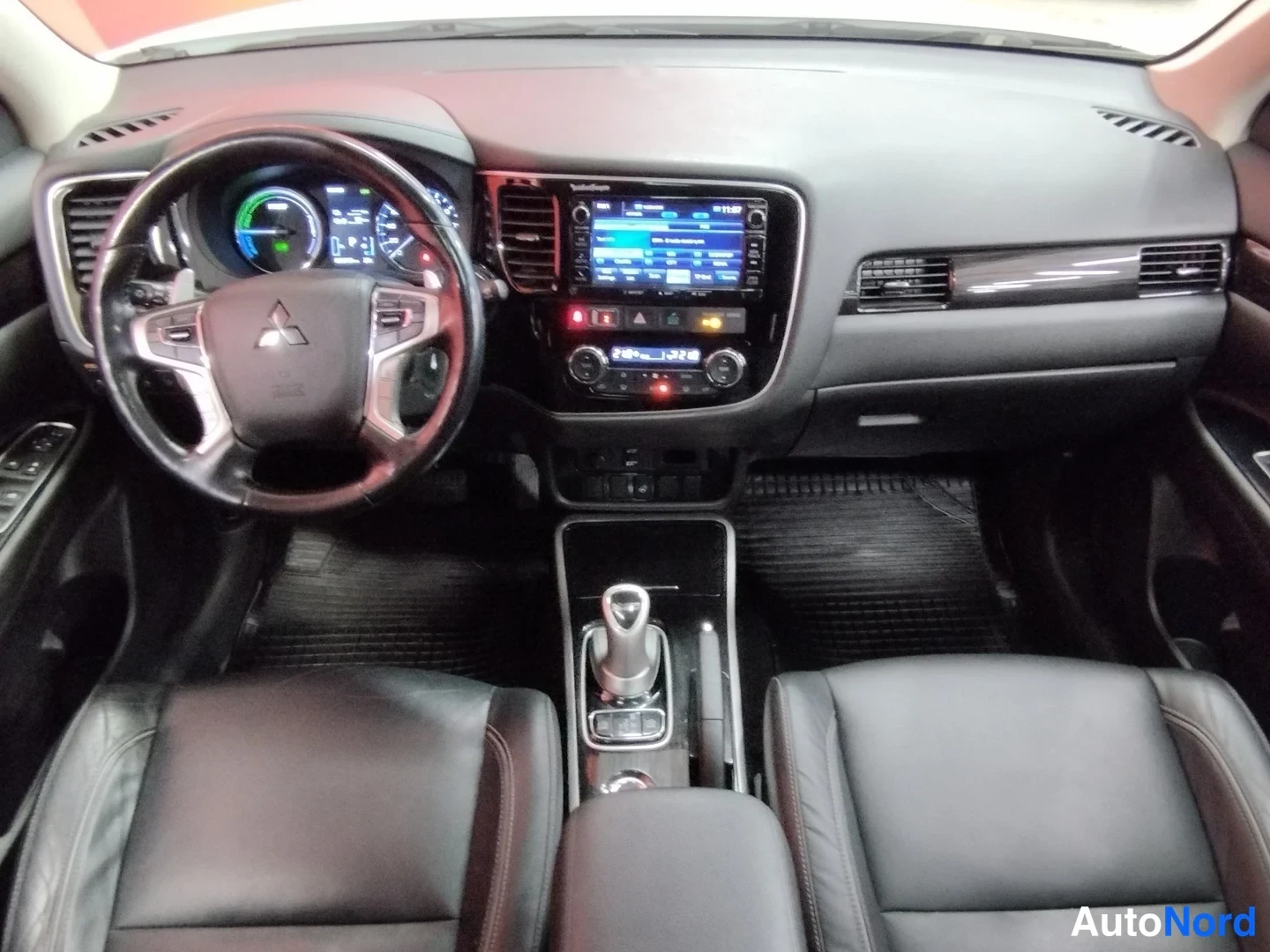 Takaa: Kojetaulun näkymä Mitsubishi Outlanderissa: monitoimiohjauspyörä, hybridin mittaristo, kosketusnäyttö ja automaattivaihteen valitsin.