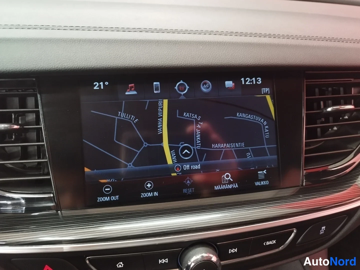 Muu: Kojeiston keskikäyttöinen infotainment-näyttö näyttää navigointikarttaa Helsingin kadunnimillä, lämpötilaa 21° ja kelloa 12:13; näytön alla ZOOM OUT-, ZOOM IN-,