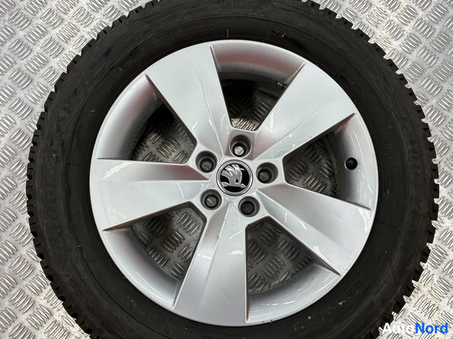 Muu: Hopeanvärinen alumiinivanne Skoda-merkillä, rengas kivijalka- tai mattopohjaisella alustalla.
