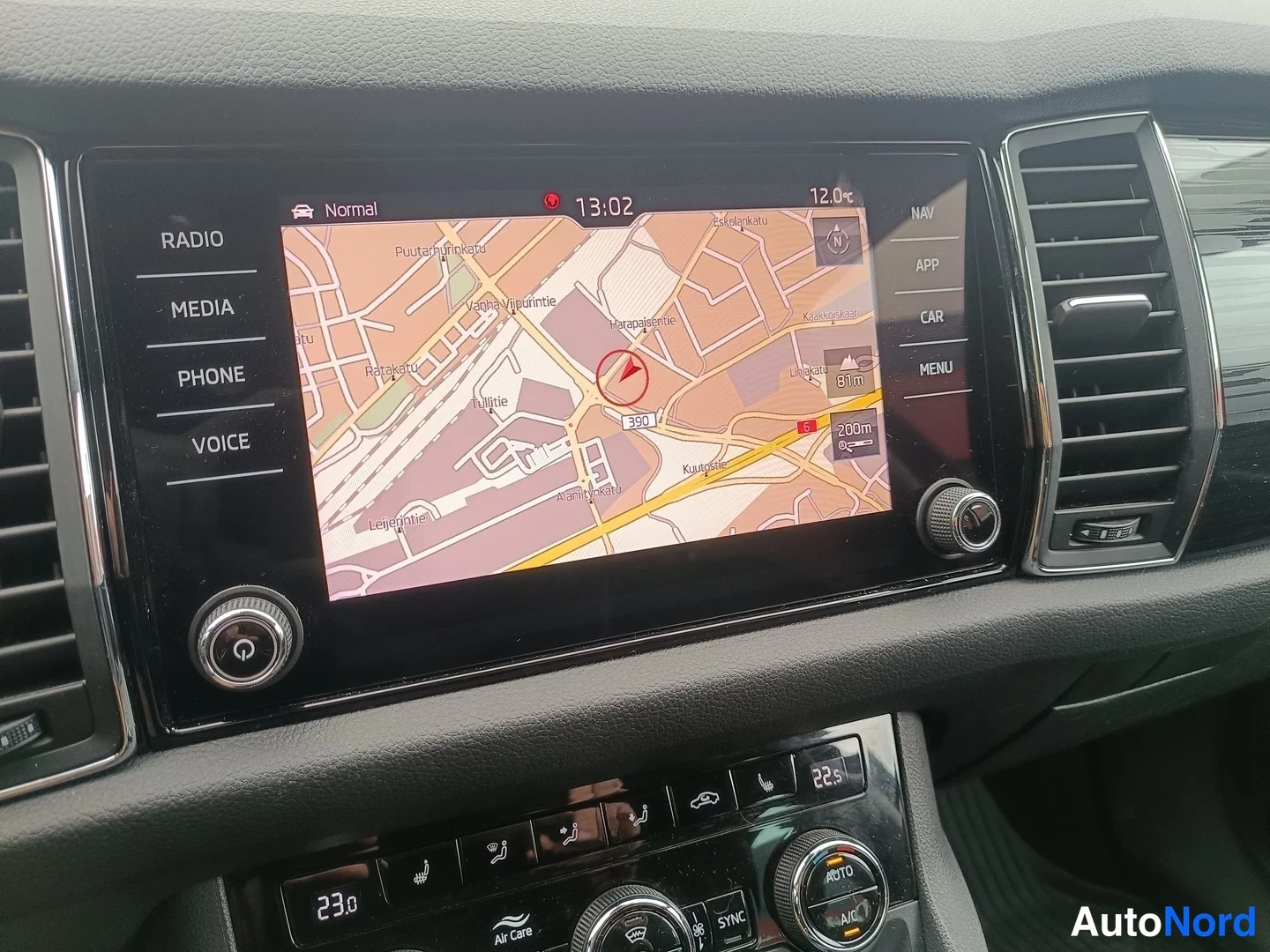 Muu: Keskikonsolin infotainment-näytöllä navigointikartta Helsingin alueelta, kello 13:02 ja lämpötila 12,0; paneelin oikealla NAV, APP, CAR ja MENU.