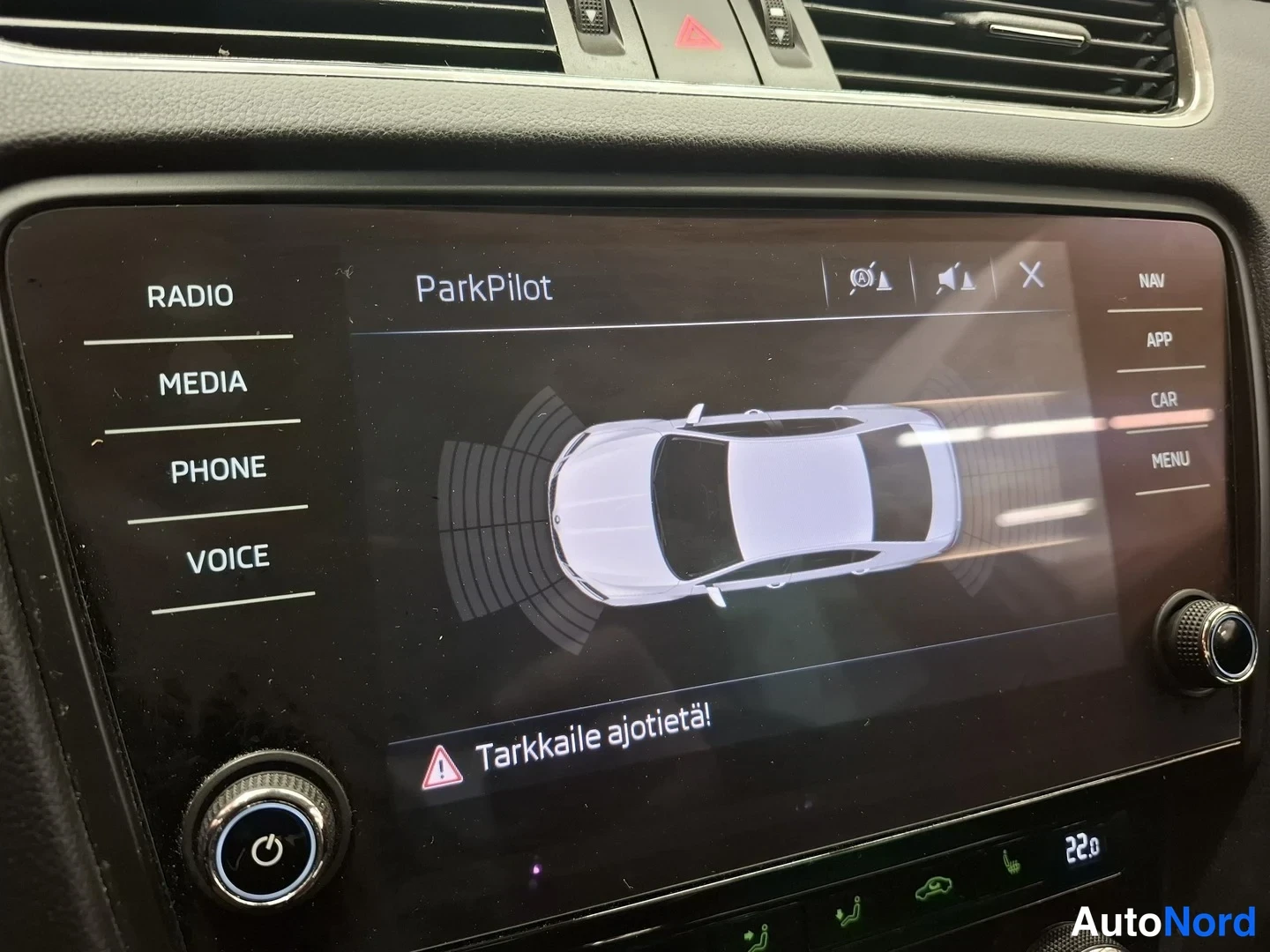 Muu: Keskikonsolin näyttö ParkPilot-tila: auto kuvattuna ylhäältä ja teksti 'Tarkkaile ajotietä!'; sivuilla RADIO, MEDIA, PHONE, VOICE, NAV, APP, CAR, MENU.