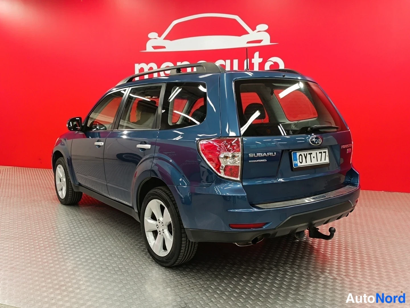 Takaviisto: Auton takakulma kuvattuna; takavalot, SUBARU-merkintä, -rekisterikilpi ja vetokoukku näkyvät punaisen taustan edessä.