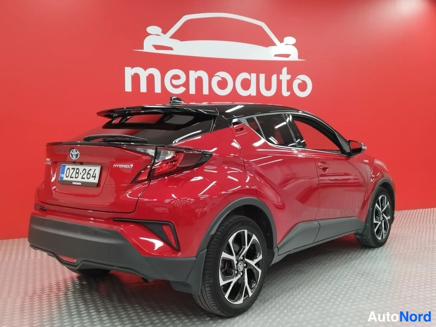 Takaviisto: Punainen Toyota C-HR takakulmasta, rekisteritunnus, takavalot ja HYBRID-teksti, musta katto, harmaassa liiketilassa punaisella taustalla.