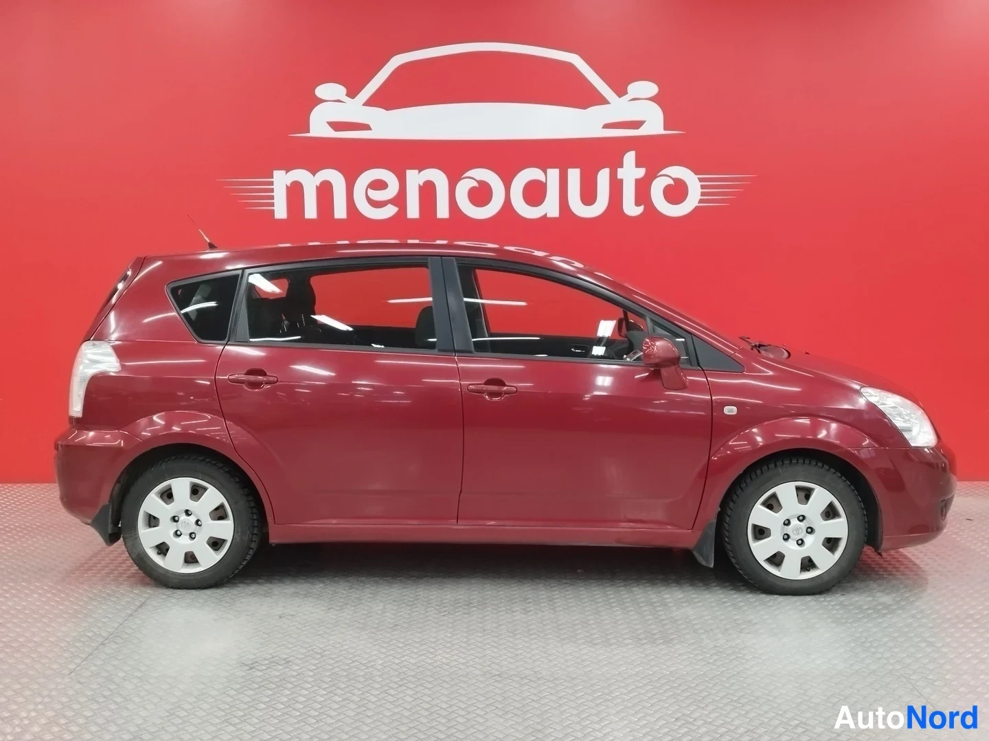 Etuviisto, nokka oikealle: Punainen Toyota Corolla Verso -pakettiauto etukulmasta oikealle, etupää ja oikea sivu näkyvissä.