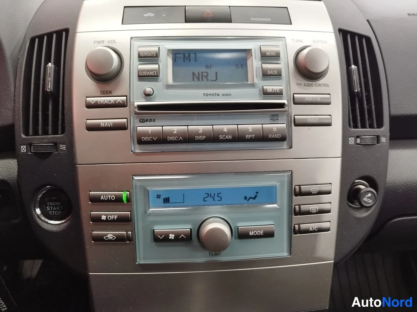 Muu: Keskikonsolin kokonaisnäkymä: Toyota-radio FM1 NRJ -näytöllä, alla ilmastointipaneeli (24,5 astetta) ja ENGINE START STOP -nappi.