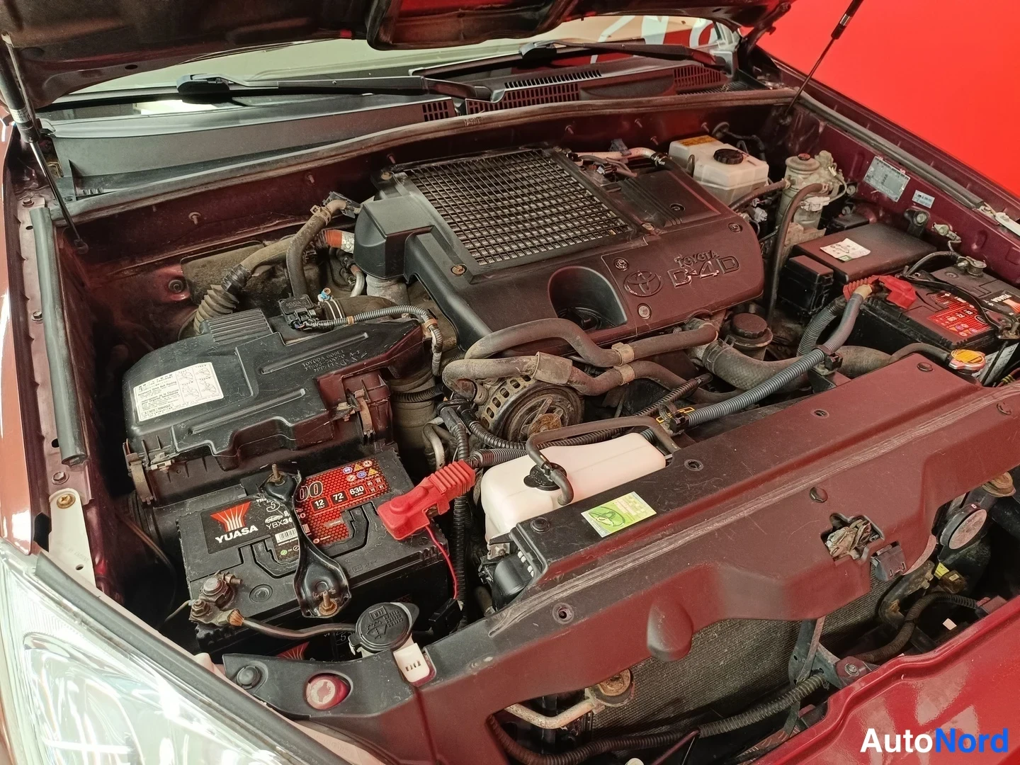 Moottoritila: Kuva Toyotan 1KD-FTV 3.0 D-4D -dieselmoottorin moottoritilasta, vasemmalla etukehällä Yuasa-akkunsa, oikealla toinen akku ja apulaitteet. Etukansi on auki.
