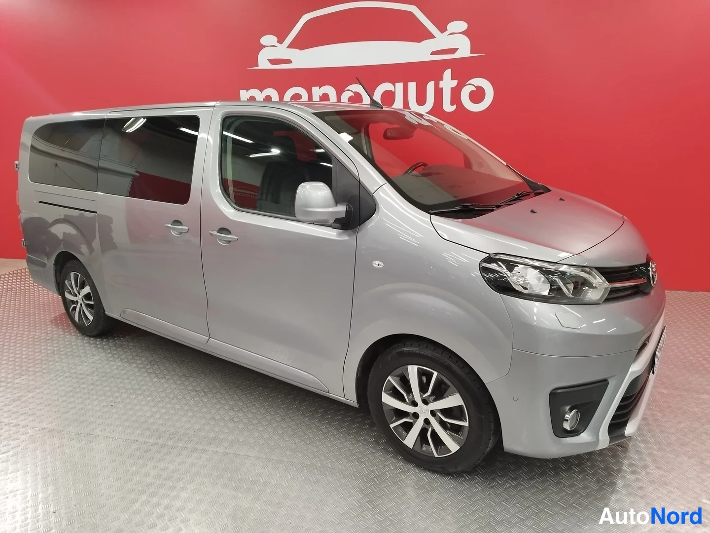 Etuviisto, nokka oikealle: Hopeaharmaa Toyota Proace Verso -pakettiauto kuvattu kolmannelta etuneljännekseltä oikealta, keulakotka ja oikea sivu näkyvät sisätiloissa punaisella tau