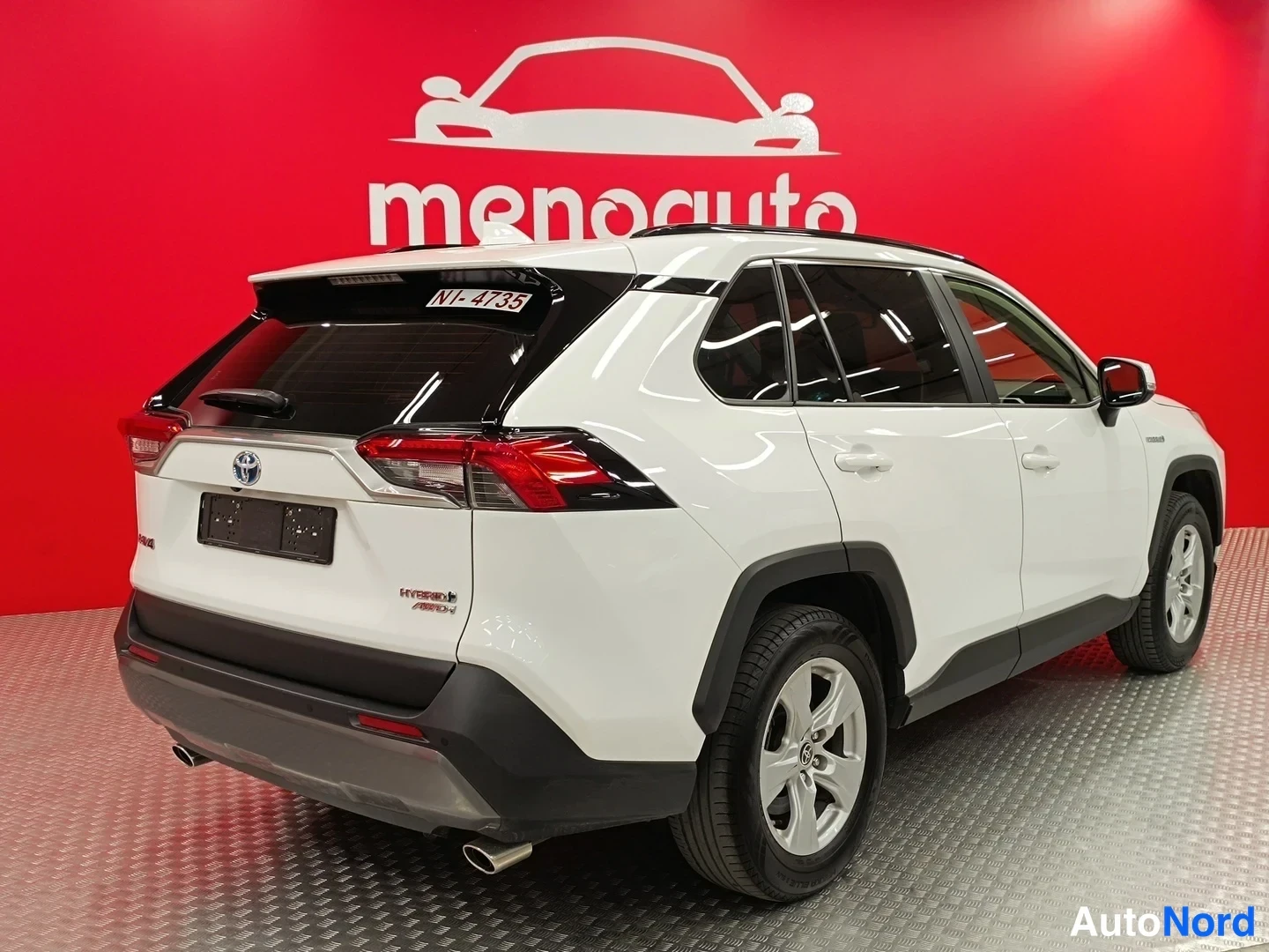 Takaviisto: Valkoinen Toyota RAV4 takaa vasemmalta, takavalot, HYBRID AWD-tarra ja rekisterikilpi näkyvissä punaisella taustalla.