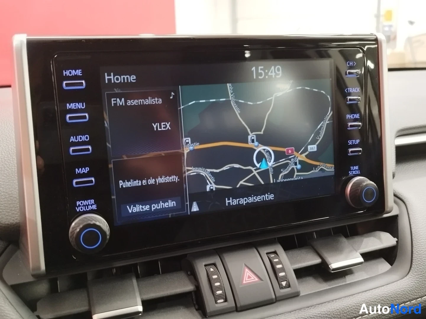 Yksityiskohta: Kojeiston kosketusnäyttö: Home-valikko, kartta ja FM-asemalista (YLEX), vasemmalla painikkeet HOME, MENU, AUDIO, MAP, POWER VOLUME, oikealla CH, TRACK, PHONE, S