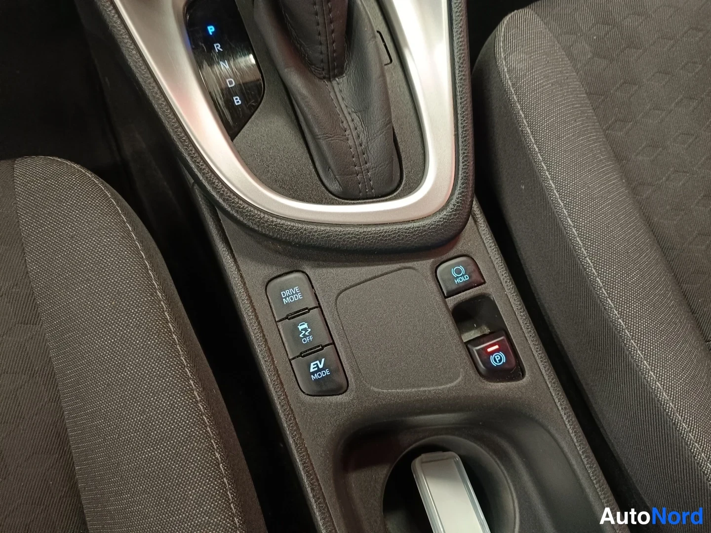Muu: Vaihteenvalitsin, jonka ympärillä lukee P, R, N, D ja B. Konsolissa ovat DRIVE MODE-, EV MODE-, HOLD- ja jarrupainikkeet, istuimet viistosti kuvassa.