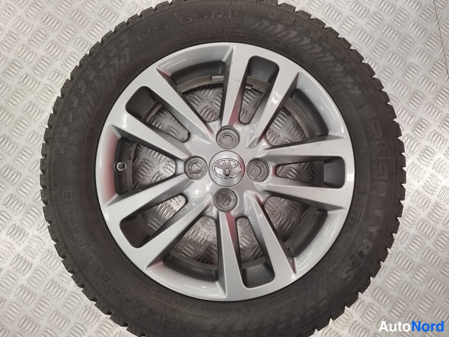 Muu: Toyota-merkillä varustettu hopeanharmaa kevytmetallivanne ja talvirengas, renkaassa lukemat 175/65R15.