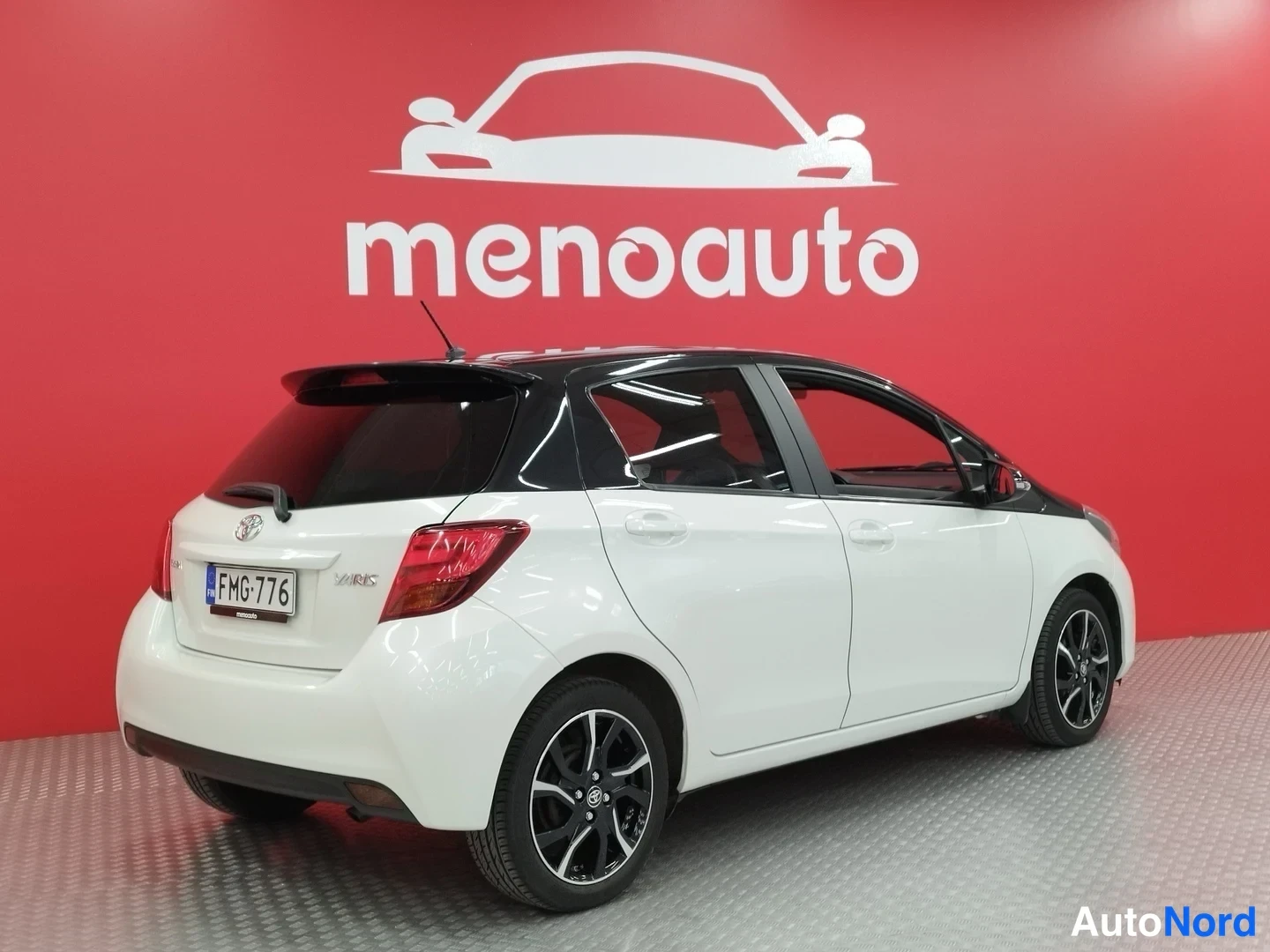 Takaviisto: Valkoinen Toyota Yaris takakulmanurikka, musta katto ja kattosiivet, takavalo ja rekisteritunnus näkyvät.