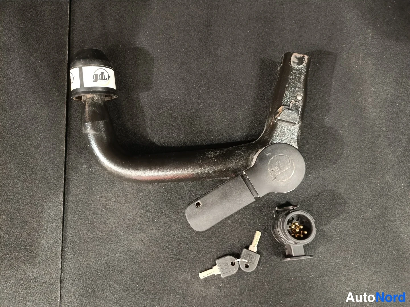 Yksityiskohta: Musta vetokoukun kaari (merkinnällä 'gob') 13-nastaisella sähköliittimellä ja kahdella avaimella tummalla taustalla.