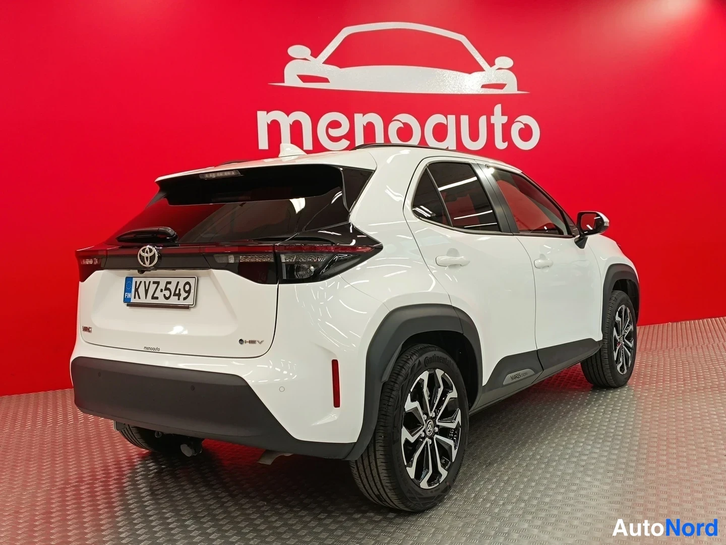 Takaviisto: Valkoinen Toyota Yaris Cross takaapäin kulmassa kuvattuna punaisella taustalla, rekisteritunnus.