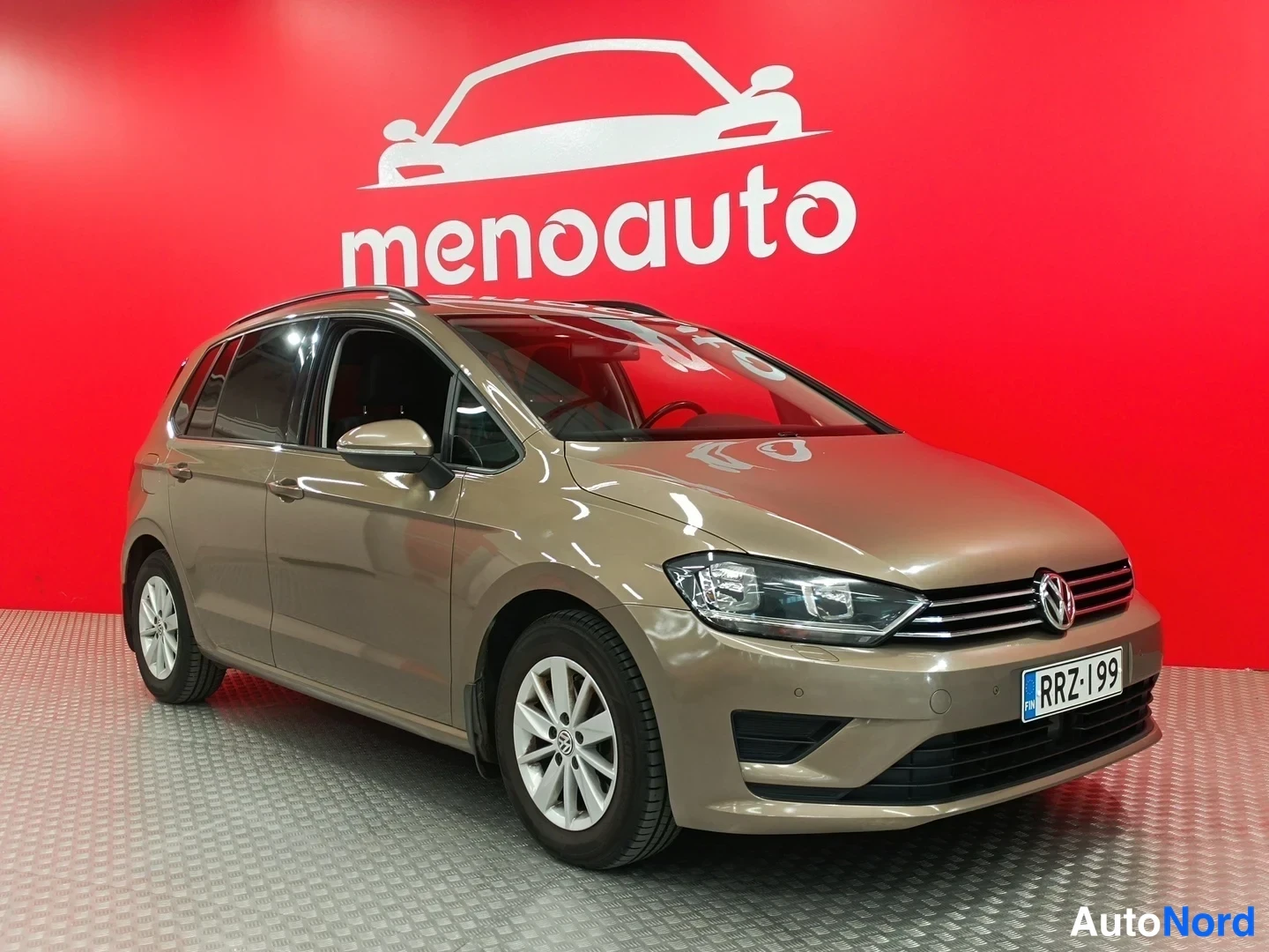 Etuviisto, nokka oikealle: Volkswagen Golf Sportsvan -farmarin auton etukulmakuva oikealta, vaaleanruskea koripelti, rekisteritunnus, punainen menoauto-taustaseinä.
