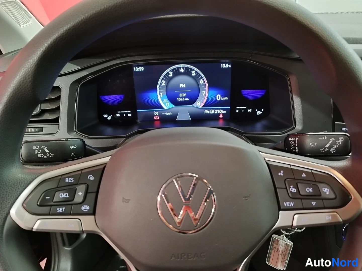 Muu: Volkswagen-ohjauspyörä ja digitaalinen mittaristo, näytöllä nopeus 0 km/h, kellonaika 13:59, ulkolämpötila 13,5 °C ja FM CITY 108,5 MHz. Ohjauspyörän vasemmassa
