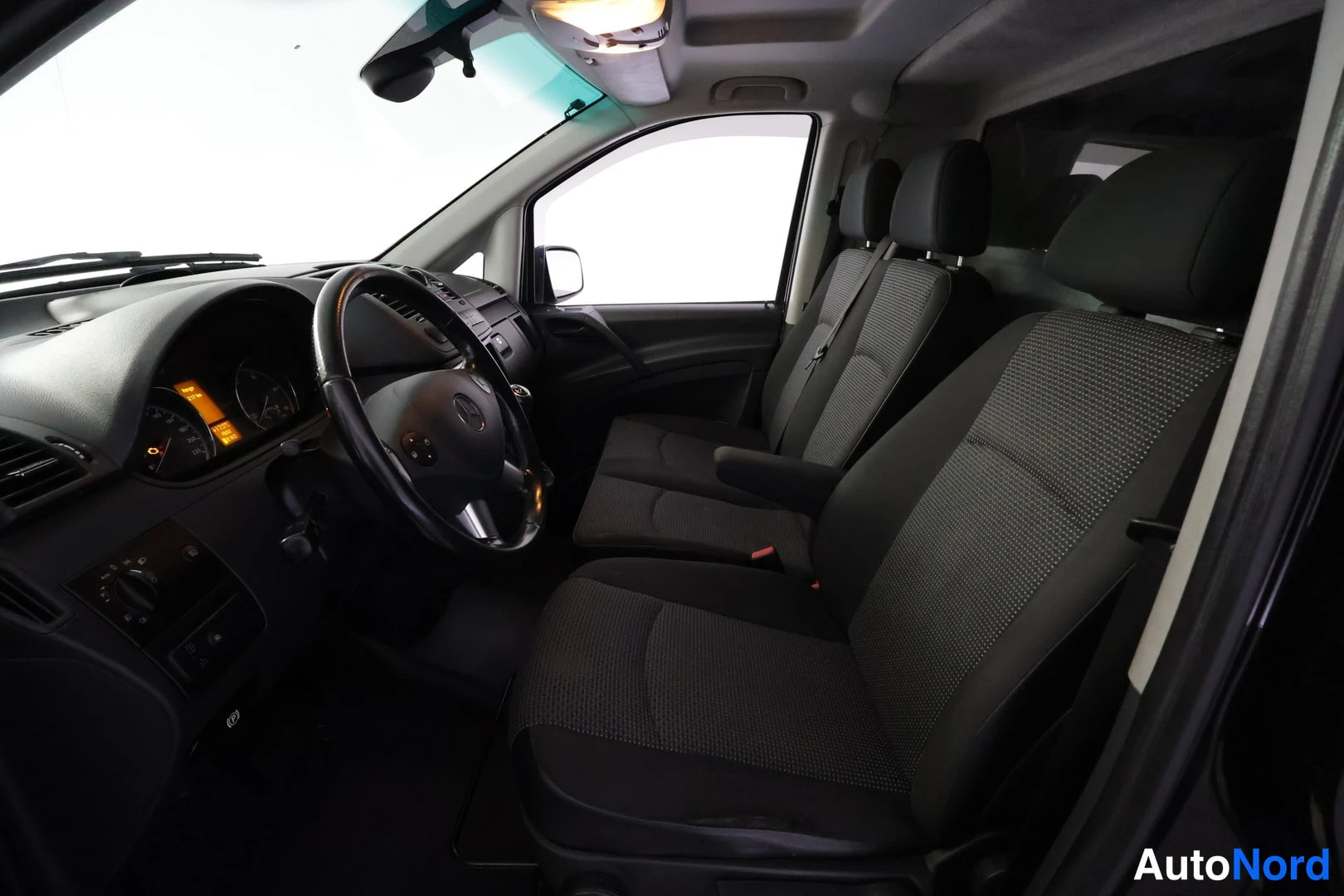 Sivulta: Ohjaamo sivusuunnassa: tummat kankaupitkä istuimet ja Mercedes-ohjauspyörä.