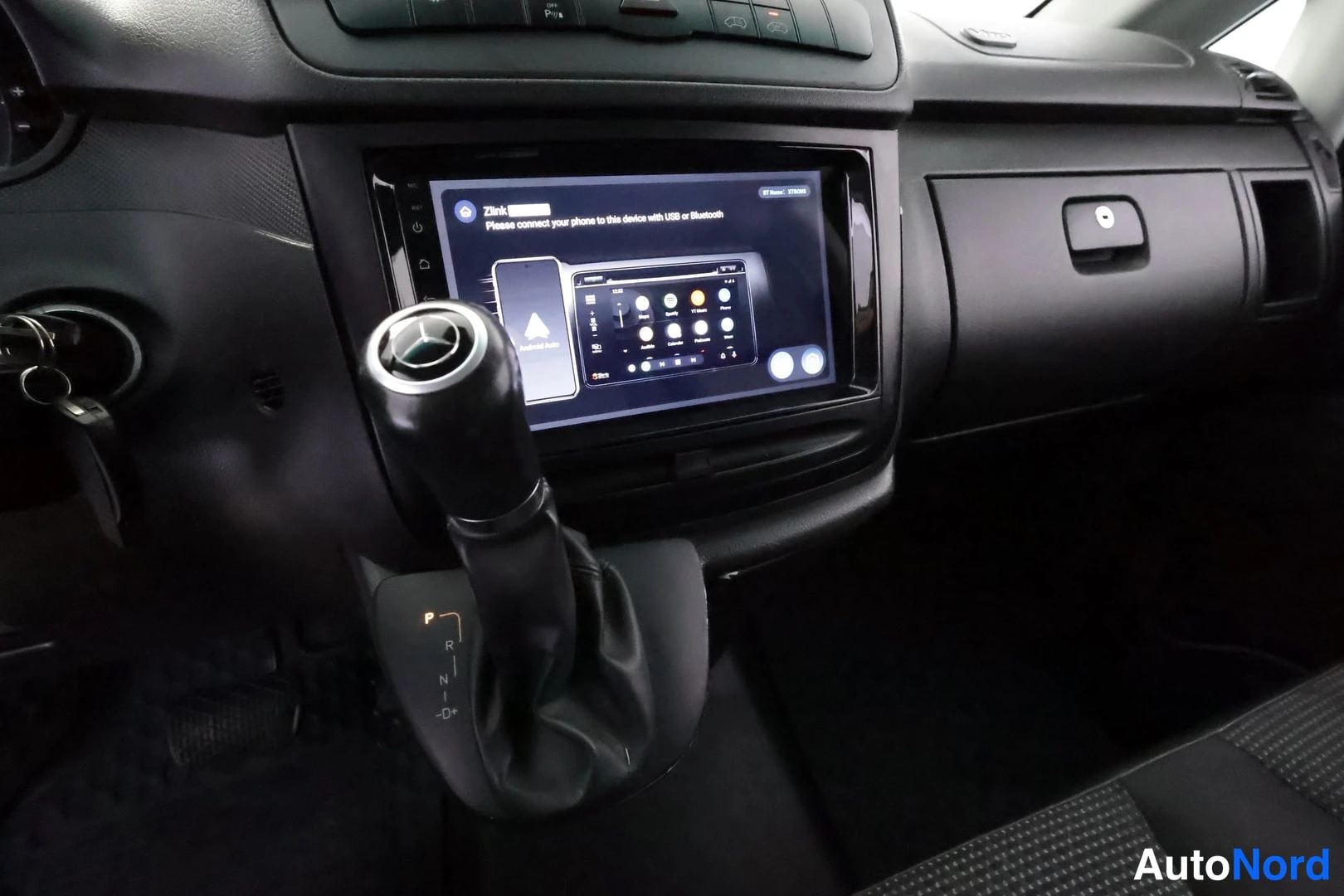 Etuviisto, nokka vasemmalle: Kojelauta ja vaihdevipu Mercedes-Benzissä, jossa 2-DIN-näytöllinen infotainment-yksikkö näyttää puhelimen yhdistämisohjeen.