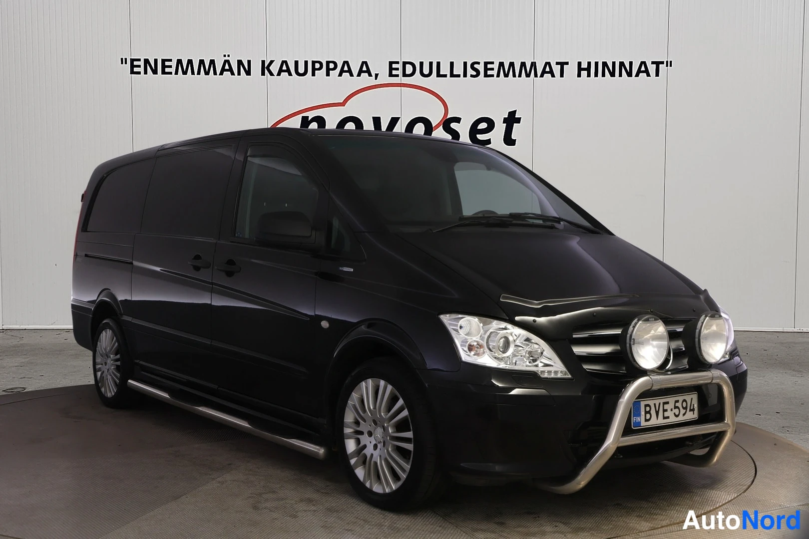 Etuviisto, nokka oikealle: Mustan Mercedes-Benz Vito -pakettiauton etukulmanäyttö: hopeinen törmäyssuoja ja lisävalot edessä, rekisteri.