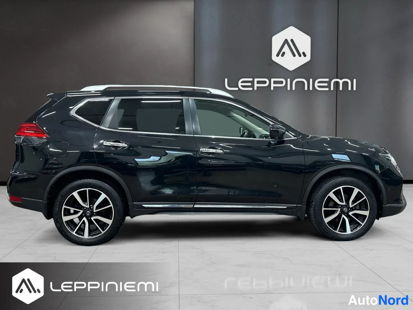 Takaviisto: Musta Nissan X-Trail takaviistosta vasemmalta sivulta, kattokaiteet näkyvissä.