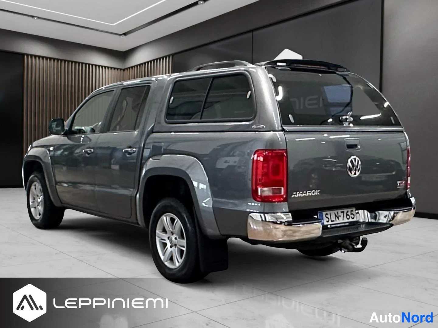 Takaviisto: Volkswagen Amarok -nella kulmasta takaa oikealta kuvattuna, tummanharmaa lava ja kova katto, takana korimerkki Amarok ja rekisterikilpi.