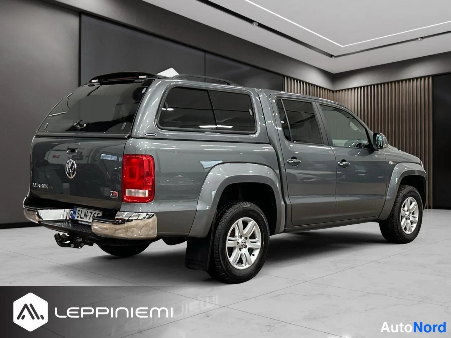 Takaviisto: Harmaa Volkswagen Amarok -avolava takaocolkulikatselmasta; takapeili, kannen takavalot ja rekisteri näkyvät.