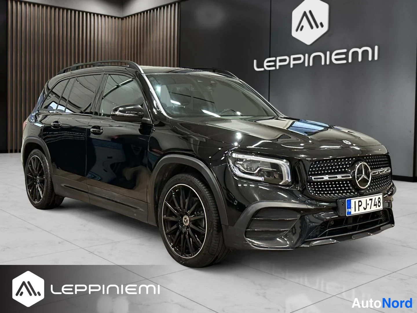 Etuviisto, nokka oikealle: Musta Mercedes-Benz GLB -maasturikaapattu edessä oikealta kolmessa neljänneksessä myyntitilassa, rekisteritunnus.