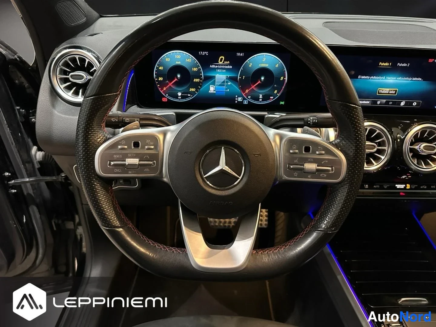 Muu: Mercedes-Benzin ohjauspyörä lähikuvassa: punotulla nahalla päällystetty ohjauspyörä, digitaalinen mittaristo ja osa MBUX-viihdejärjestelmän ruudusta.