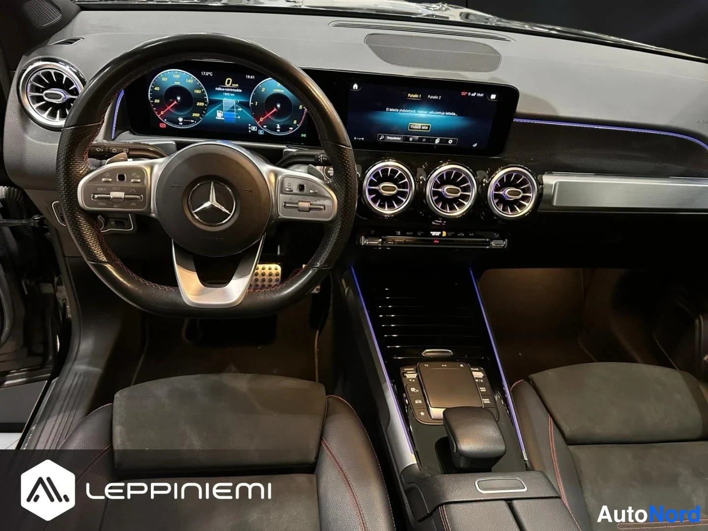 Muu: Mercedes-Benzin ohjaamo suoraan edestä kuvattuna: ohjauspyörä, digitaalinen mittaristo, keskikäyttötaulu kolmella pyöreällä tuuletusaukolla ja kosketusohjaimell