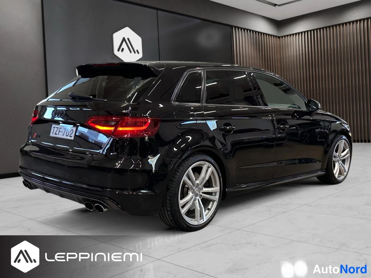 Takaviisto: Mustan Audi S3 Sportbackin takakolmasnäkymä showroomissa; takavalo, takapuskuri ja sivuprofiili näkyvissä.