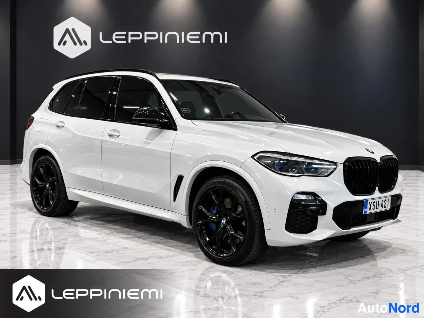Etuviisto, nokka oikealle: Valkoinen BMW X5 etukulmasta oikealta, mustat kevytmetallivanteet ja musta etusäleikkö, rekisterikilpi.