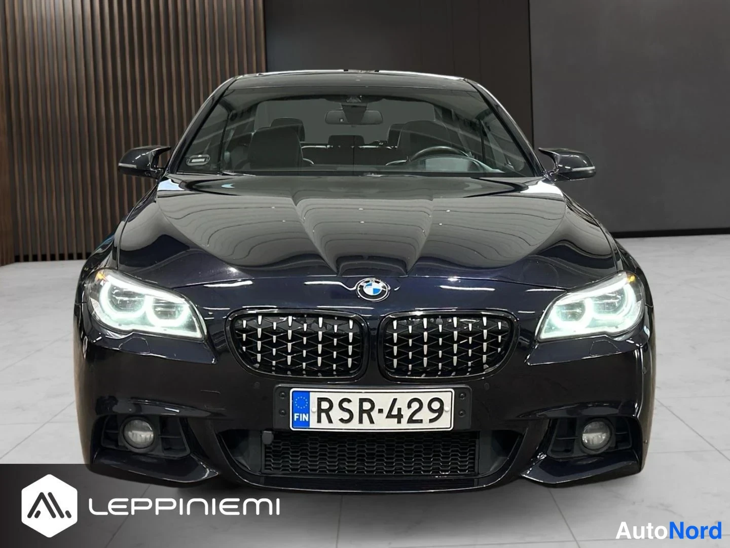 Edestä: BMW-sedan suoraan edestä kuvattuna, LED-ajovalot päällä, rekisteritunnus.