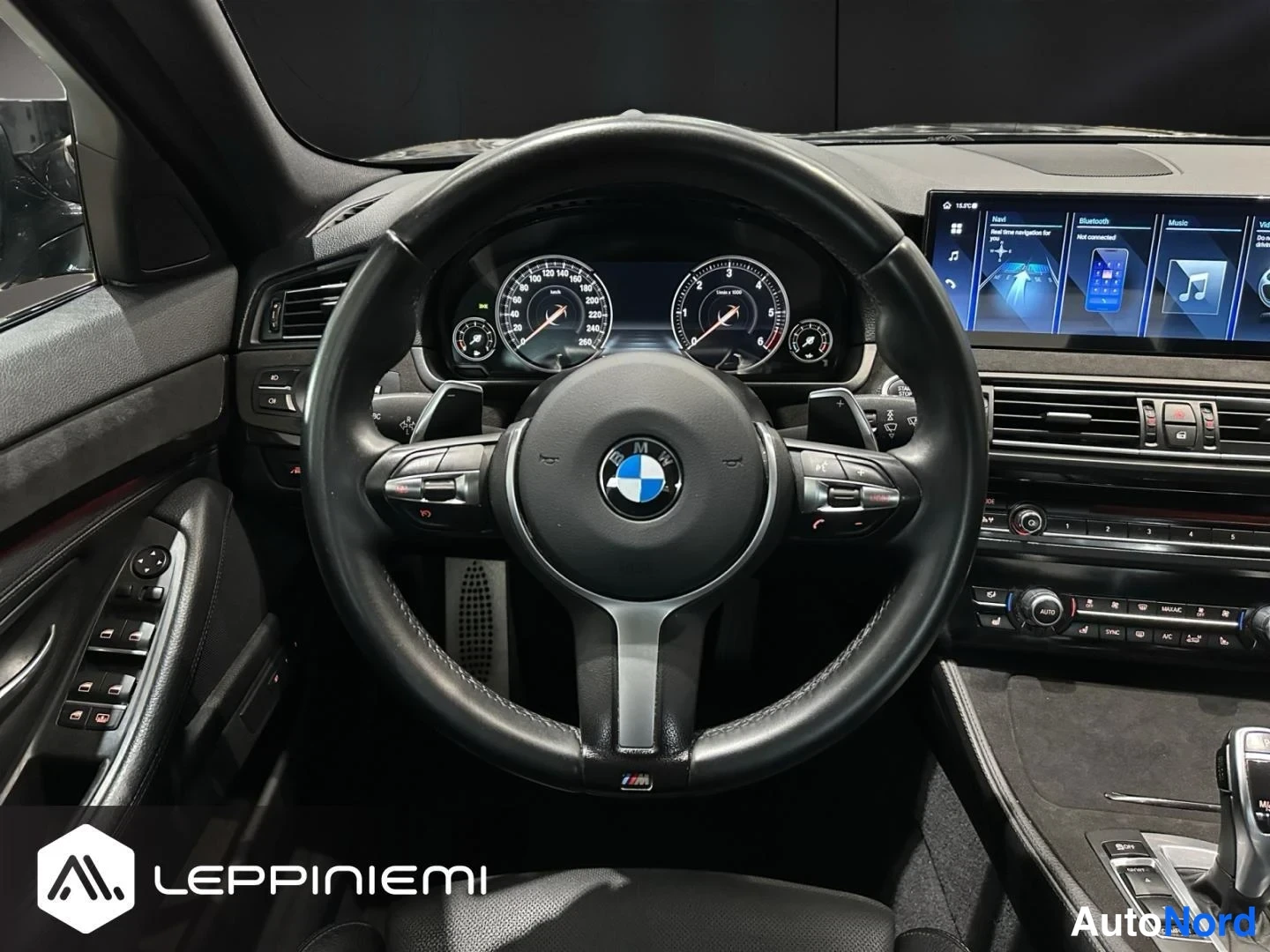 Muu: Ohjauspyörän lähikuva BMW:n sisätiloissa: M-ohjauspyörä, mittaristo ja kojelaudan näyttö.