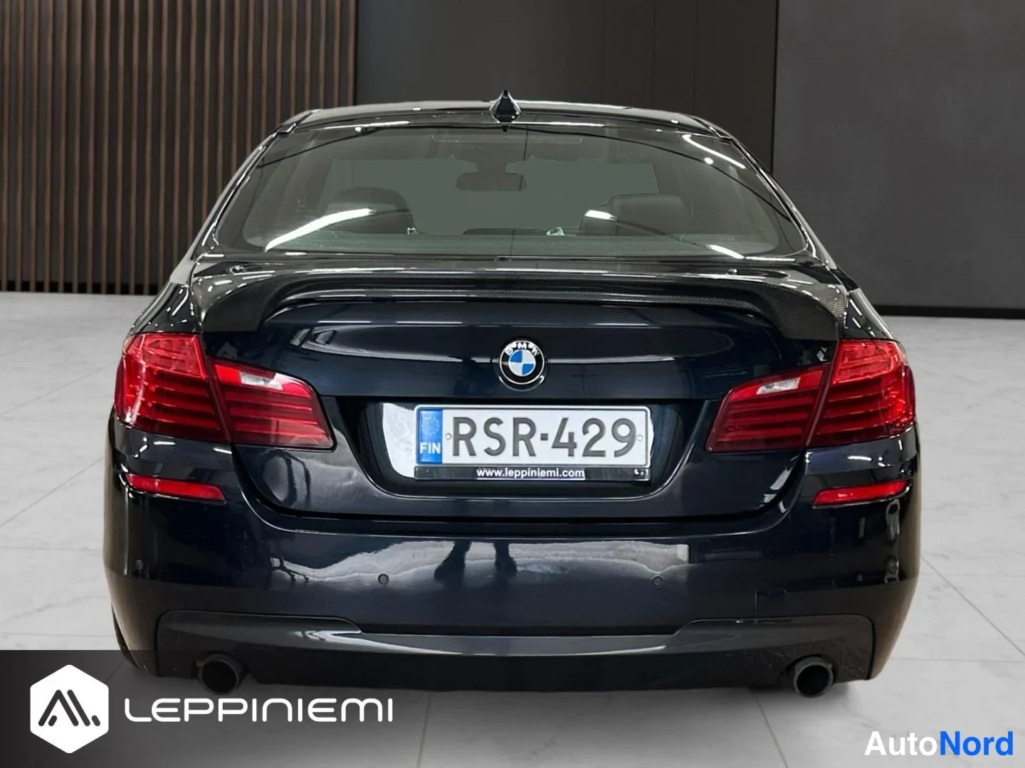 Takaa: Suora takanäkymä tummansinisen BMW 5-sarjan sedaanin perästä, rekisterikilpi.
