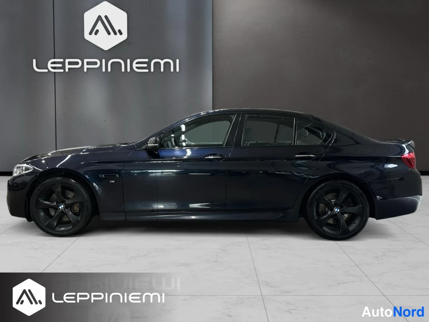 Sivulta: Sivuprofiilikuva tummansinisen BMW 5-sarjan sedaanin vasemmasta sivusta, mustat vanteet.