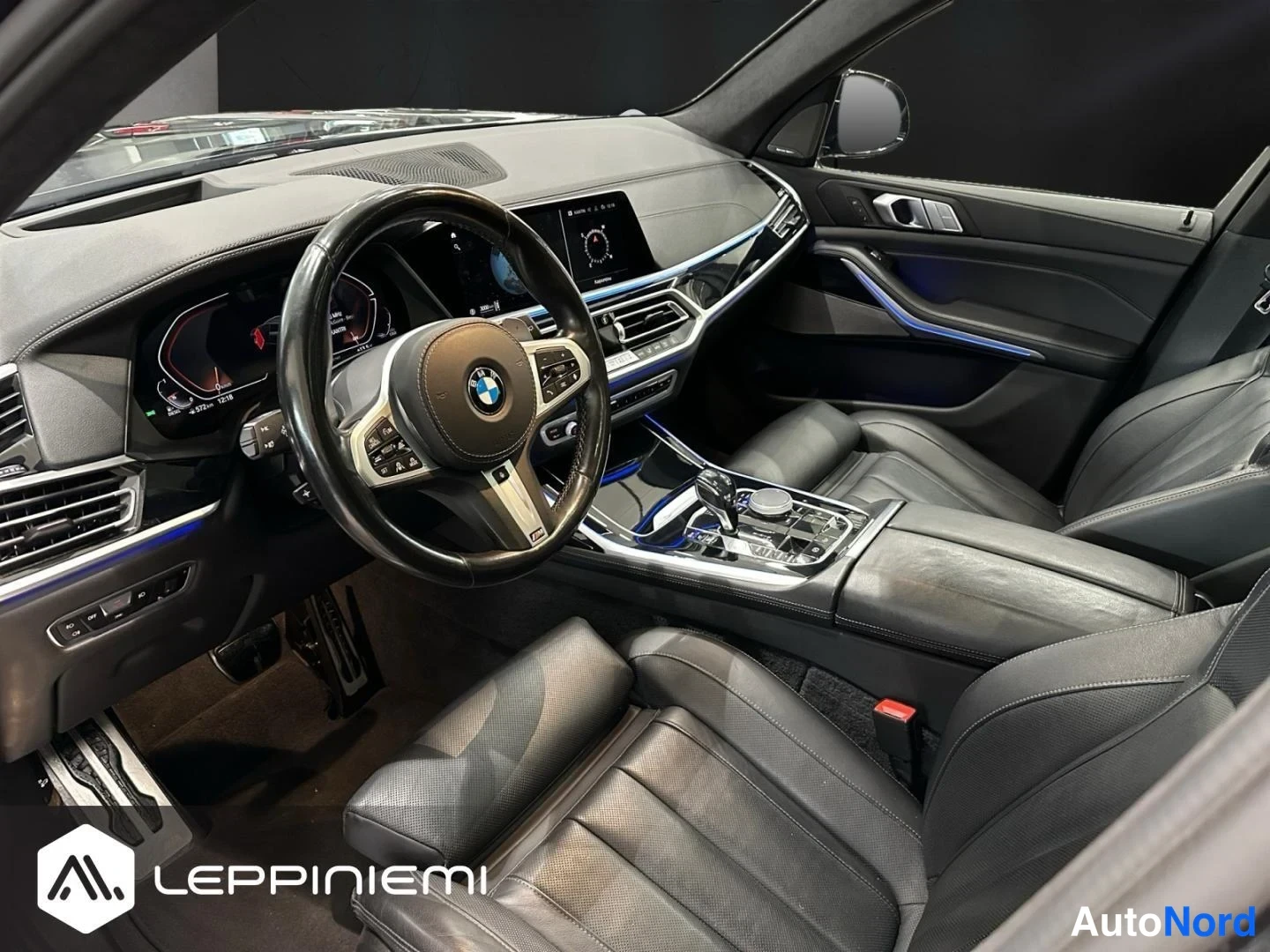 Yksityiskohta: BMW:n ohjaamo sivulta kuvattuna: nahkaverhoillut istuimet, M-ohjauspyörä, digitaalinen mittaristo, keskikonsolin vaihtajanuppi ja tunnelman valaistus.