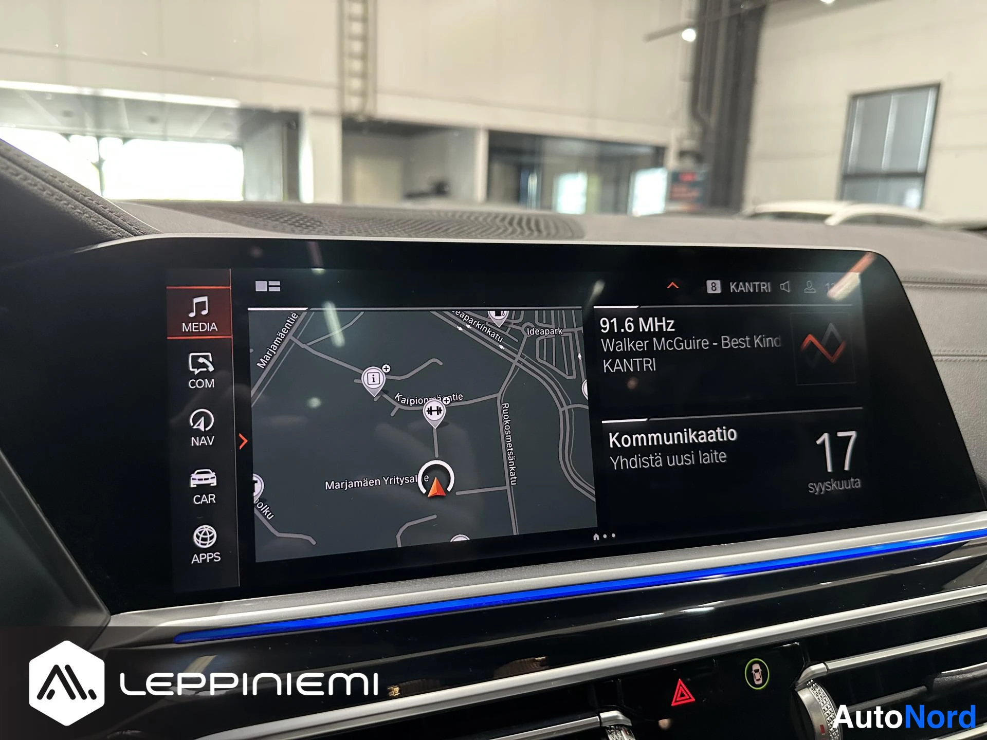 Yksityiskohta: Kojelaudan keskellä oleva viihdejärjestelmän näyttö: vasemmalla MEDIA-, COM-, NAV-, CAR- ja APPS-valikot, karttanäkymä, oikealla radio 91.6 MHz (Walker McGuire,