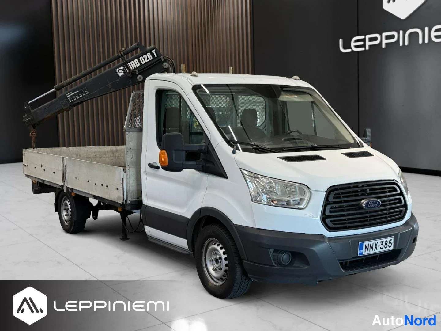 Etuviisto, nokka oikealle: Valkoinen Ford Transit -lava-auto kulmassa edestä oikealta, HIAB 026 T -kuormanosturi lavalla, rekisteri.