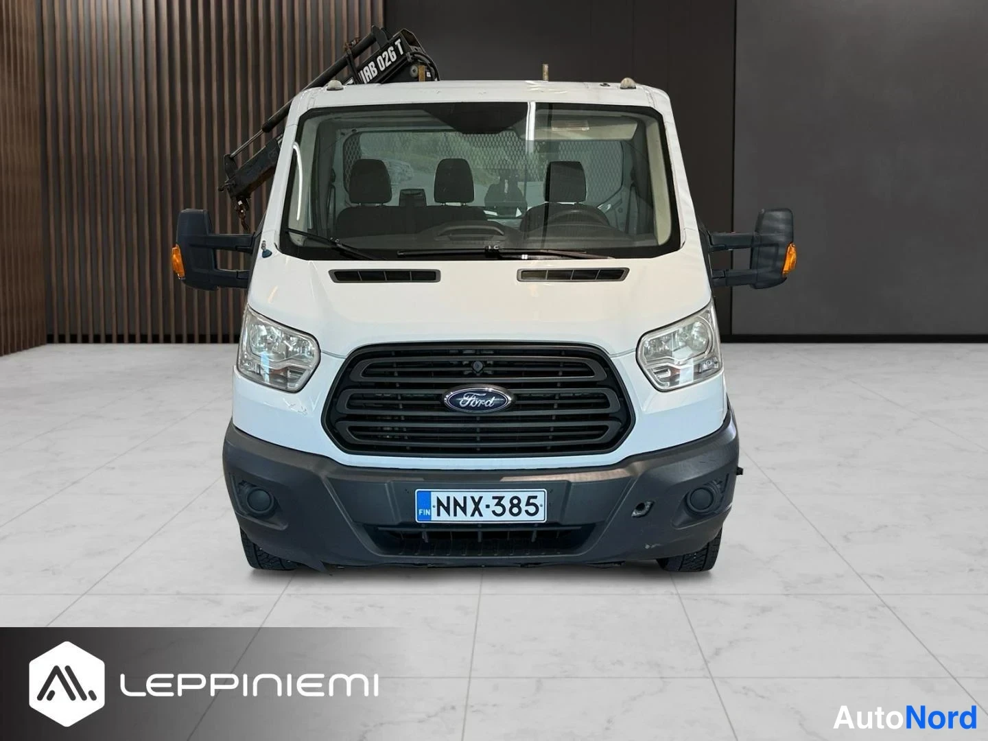 Edestä: Valkoinen Ford Transit suoraan edestä, HIAB 026 T -nosturin tarttuma-arm yltää ohjaamon yli, rekisteri.