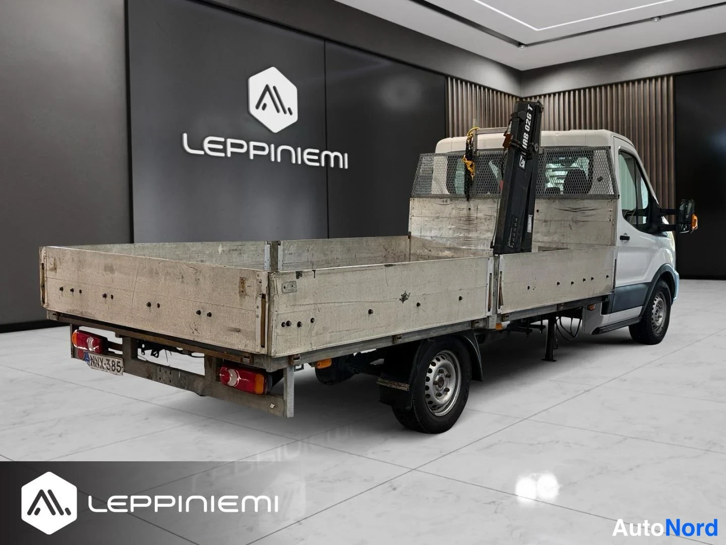 Takaviisto: Valkoinen Ford Transit -avolava takaviistosta; lava on tyhjä, HIAB 026 T -nosturi lavan edessä ja rekisterikilpi takassa.