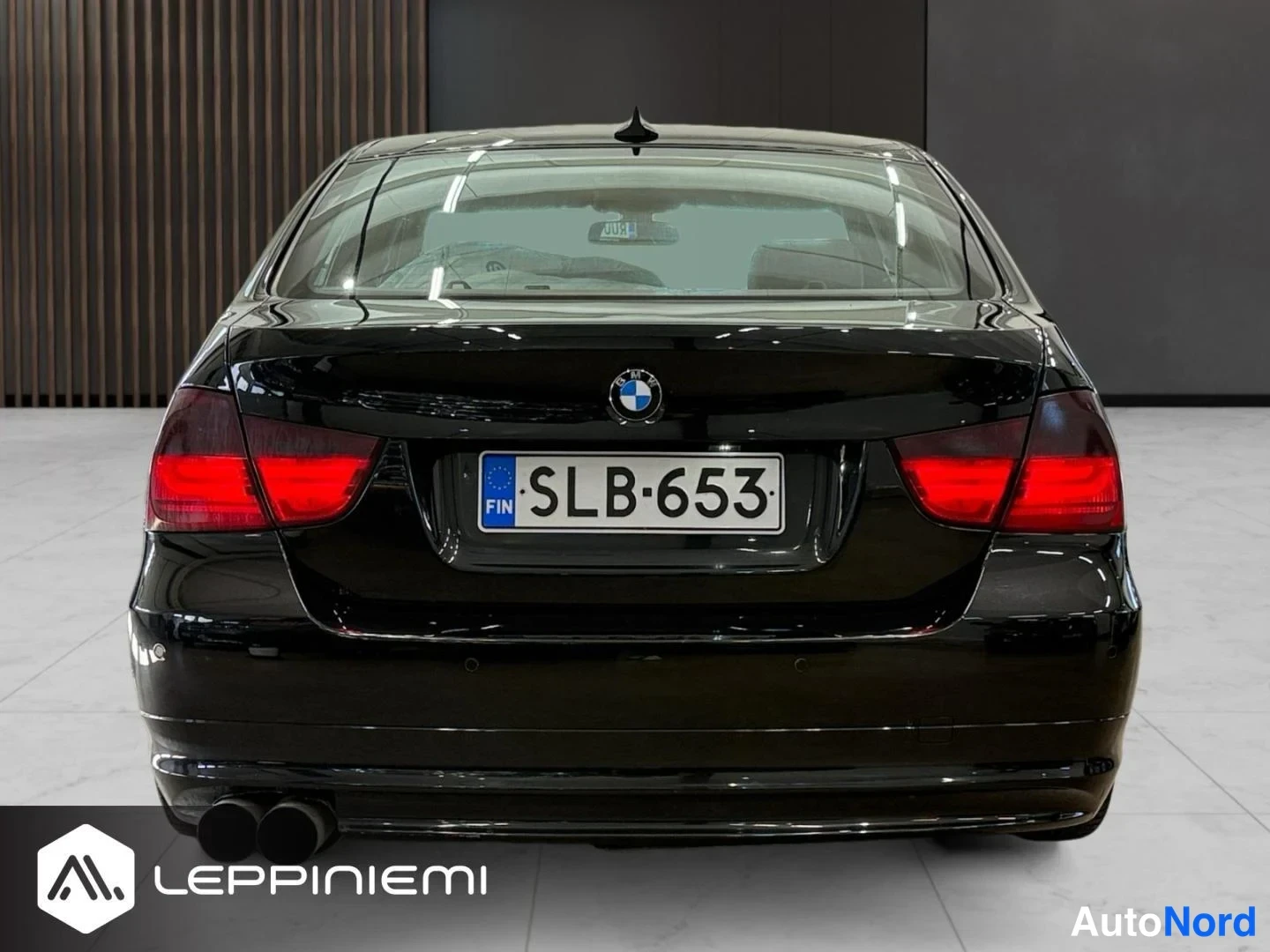 Takaa: Mustan sedanin takaosa suoraan takaa; näkyvissä takavalot, rekisterikilpi, BMW-embleemi ja kaksiosainen pakopää.