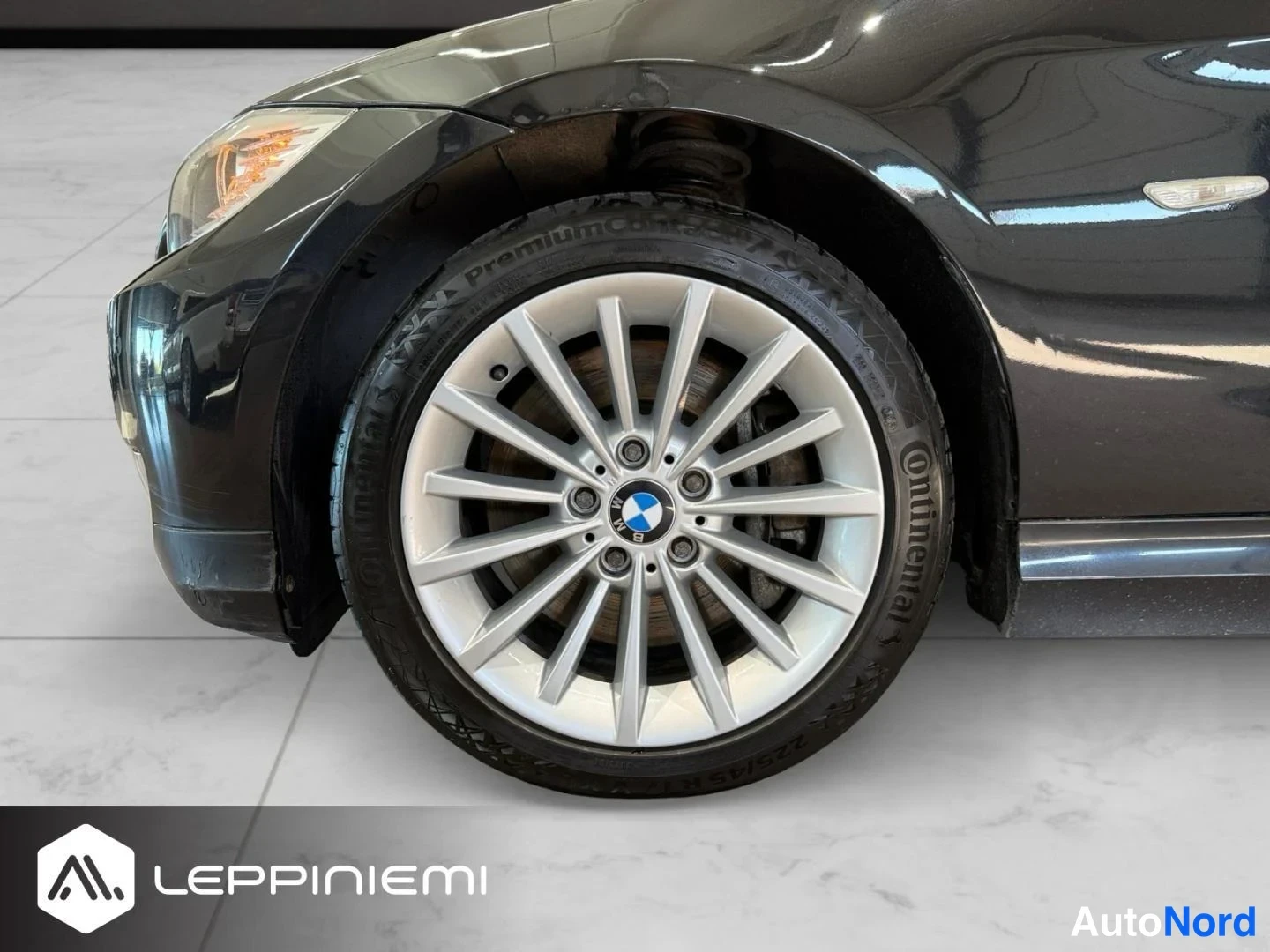 Etuviisto, nokka vasemmalle: BMW:n etuvasen pyörä lähikuvassa, hopea pulttikiinnitteinen vanteen ja Continental-renkaan alla; etusumuvalo ja tumma kylki näkyvät.