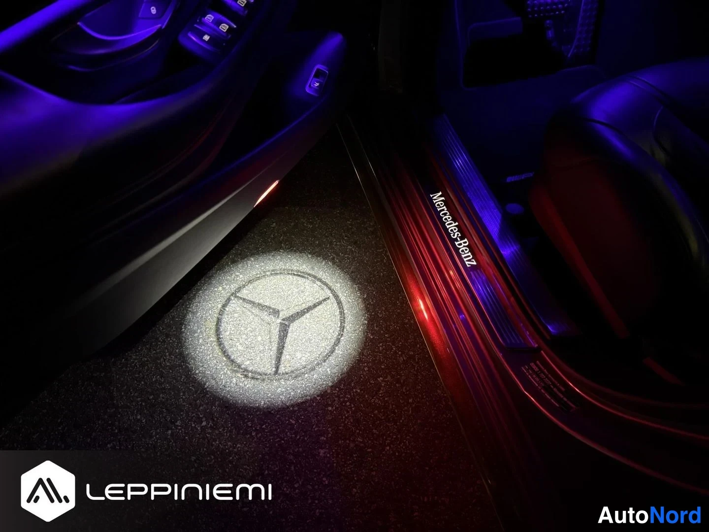 Yksityiskohta: Avoimen oven kynnys, jossa on Mercedes-Benz-teksti ja kilpi heijastettuna lattiaan.