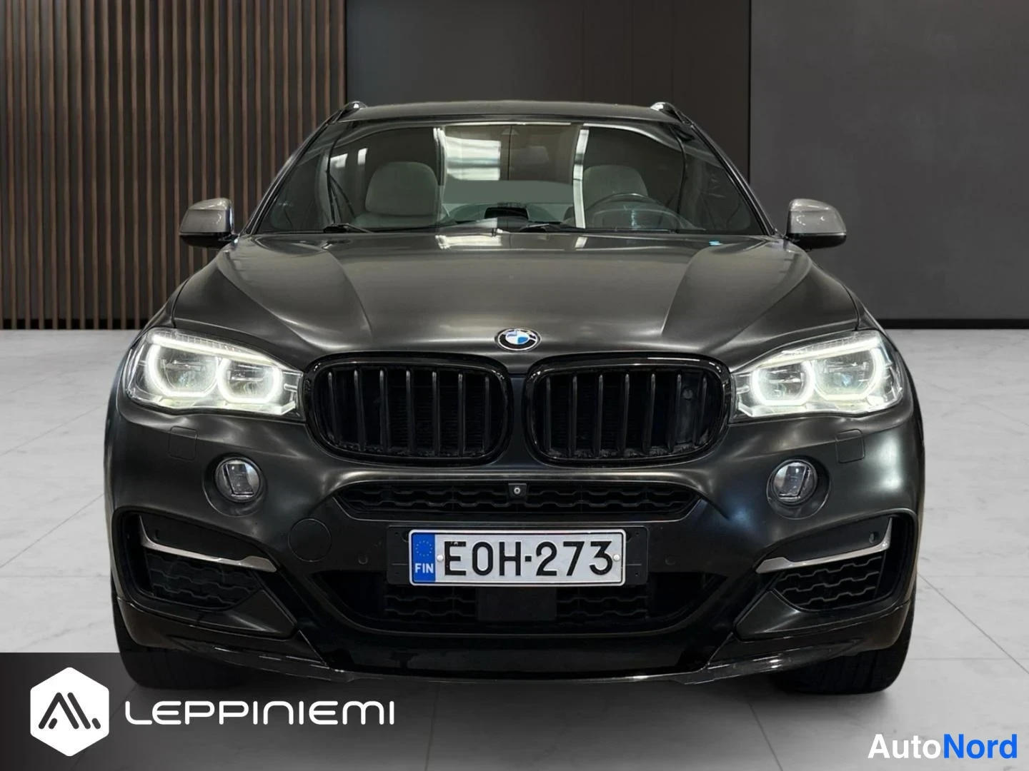Edestä: Musta BMW X6 suoraan edestä kuvattuna, BMW-merkki ja rekisterikilpi E0H-273 näkyvät.